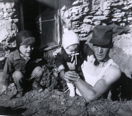 Wendel Ferrin holds his 2nd son, Jerry, while his oldest son, Darrell, squats beside them. Taken at the Ferrin farm, Comanche County, Kansas, December 1952, while Wendel was digging a celler which adjoined the bathroom to hold a water pump and hot water heater.