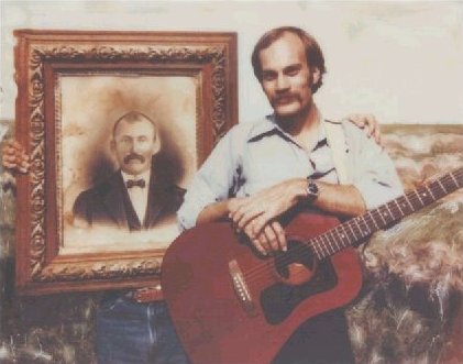 Jerry Ferrin, taking a break from playing guitar at a Ferrin family reunion at Buck Ferrin's house in Comanche County, Kansas, poses with a photo of his great grandfather, Loren Ferrin.  Polaroid photo by Wendel Ferrin, 1984.