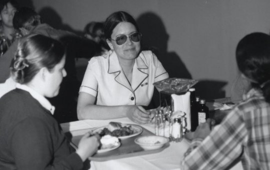 Pat Garlic in her dress white USN uniform dines with two friends at the 1975 Miss NPTR dinner at the enlisted chow hall at the National Parachute Test Range, El Centro, California, circa 1975. Pat married PHAN Tim Nagel. The woman in a plaid shirt at right with her back to the camera is Sheila Sweeney, Miss NPTR of 1974. Sheila was an NPTR air controller.

Photo by PHAN Pat 'Smitty' Smith.