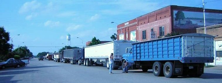 Line of Wheat Trucks in Protection, Comanche County, Kansas, 15 June 2005. A mural by Stan Herd is on the building at right.  Photo by Orlin Loucks.

(View looking north.)