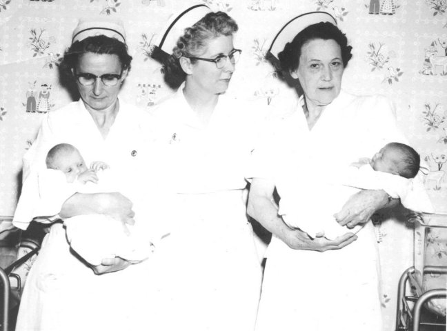 Three Registered Nurses at the Comanche County Hospital, Coldwater, Kansas, 1954. 

Left to right are Mrs. Edith (Cline) Martin, a graduate of the Christian Axtell Hospital, Newton, Kansas; Mrs. Clyde (Thelma) Blackard, hospital superintendent, a graduate of Wesley Hospital, Wichita; and Mrs. Frank (Palvena) Barnhart of Protection, a graduate of the City Hospital, Denison, Texas. 

Mrs. Barnhart is holding Patricia Jean Snyder, daughter of Mr. And Mrs. Carl Snyder Jr. of Wilmore and Mrs. Martin is holding Beverly Ann Hackney, daughter of Mr. And Mrs. Robert Hackney of Wilmore. 

The 18 employees of the hospital include Miss Pearl Gerhart who, starting March 1, 1954, is the full-time receptionist and bookkeeper.

Photo courtesy of Martin Sizemore.