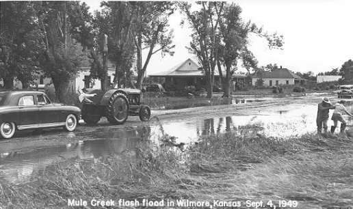 Main Street after the Mule Creek flash flood of Sept 4, 1949. At right, Harve Schrock helps his grand-daughter, Janet, to secure footing. Wilmore, Comanche County, Kansas. Photo by John Edward (Ed) Schrock, used with permission of Janet Schrock Hubbard.